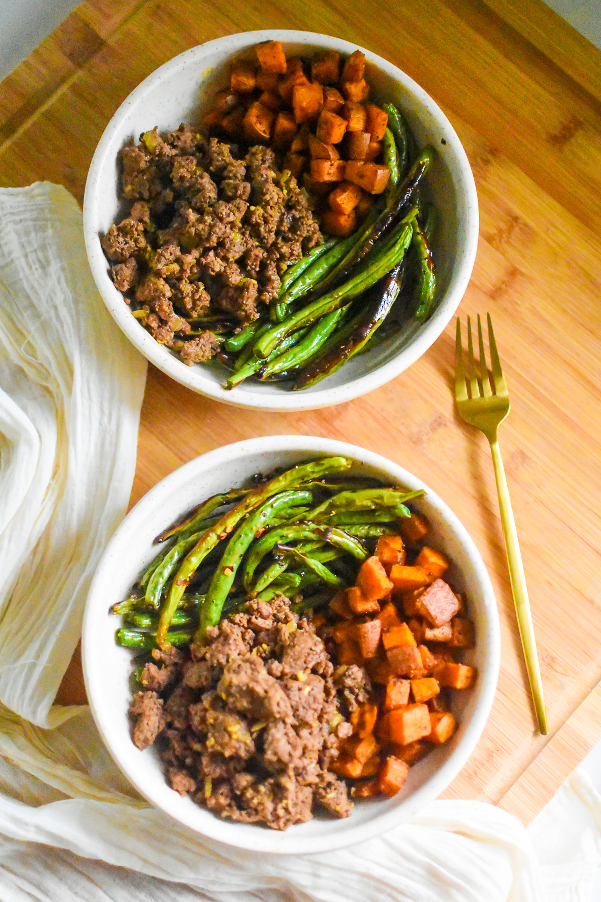 two ground beef dinner bowls with seasoned lean ground beef, roasted sweet potatoes, and roast green beans.