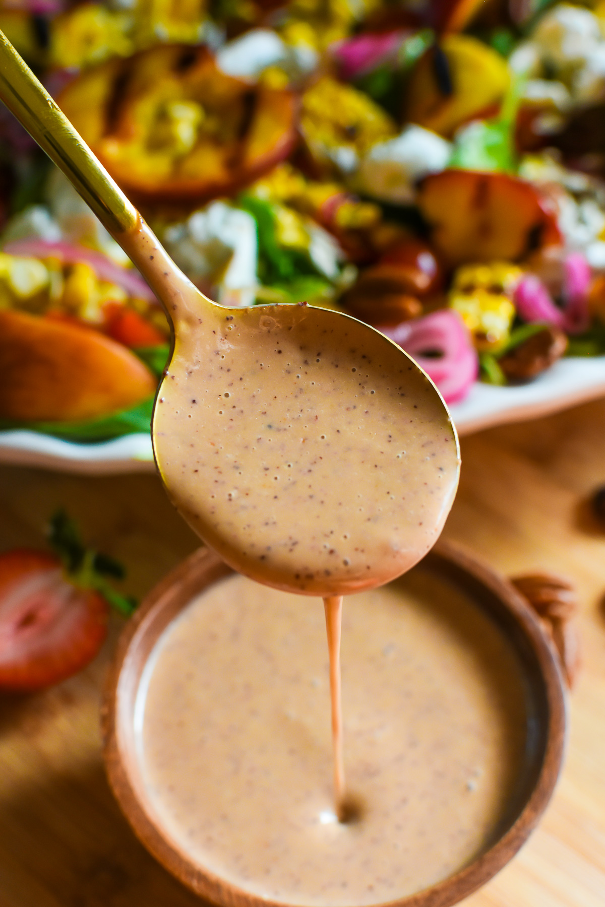 freshly made strawberry and chive summer salad vinaigrette with poppy seeds dripping from a gold spoon into a wooden bowl.