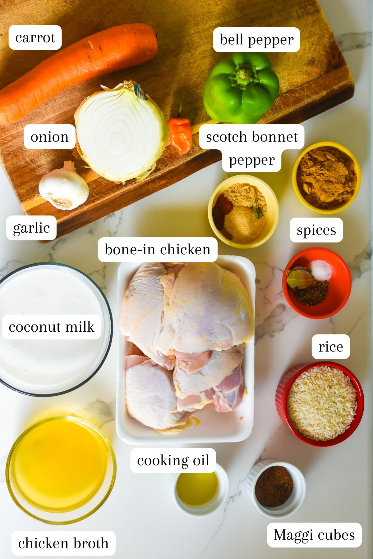 ingredients for a coconut curry chicken and rice recipe on counter top: carrot, green bell pepper, scotch bonnet pepper, onion, garlic, spices, coconut milk, bone-in chicken thighs, long-grain rice, chicken broth, cooking oil, and maggi cubes.