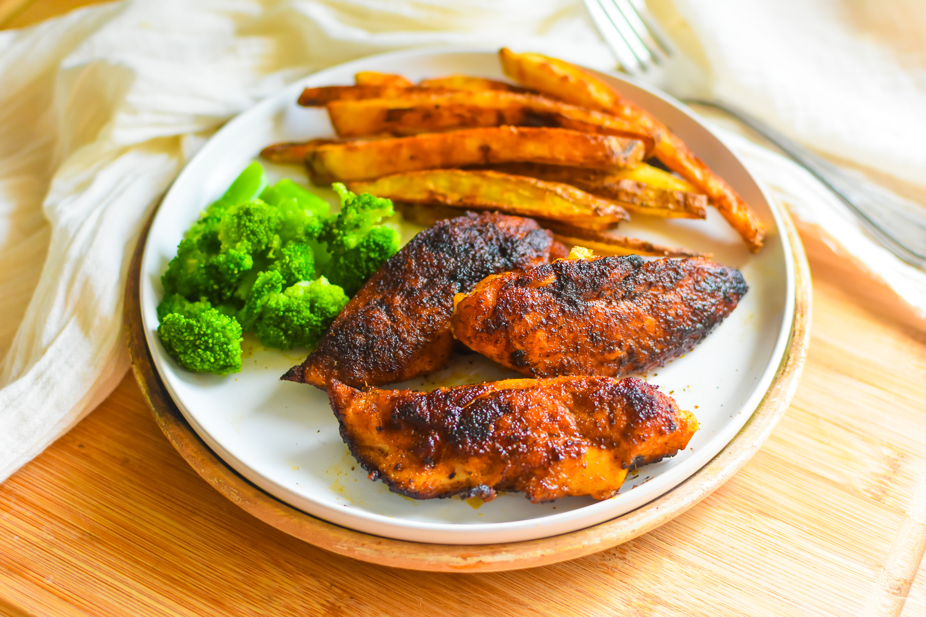 dinner plate with three blackened chicken tenders, broccoli florets, and crispy roasted French fries.