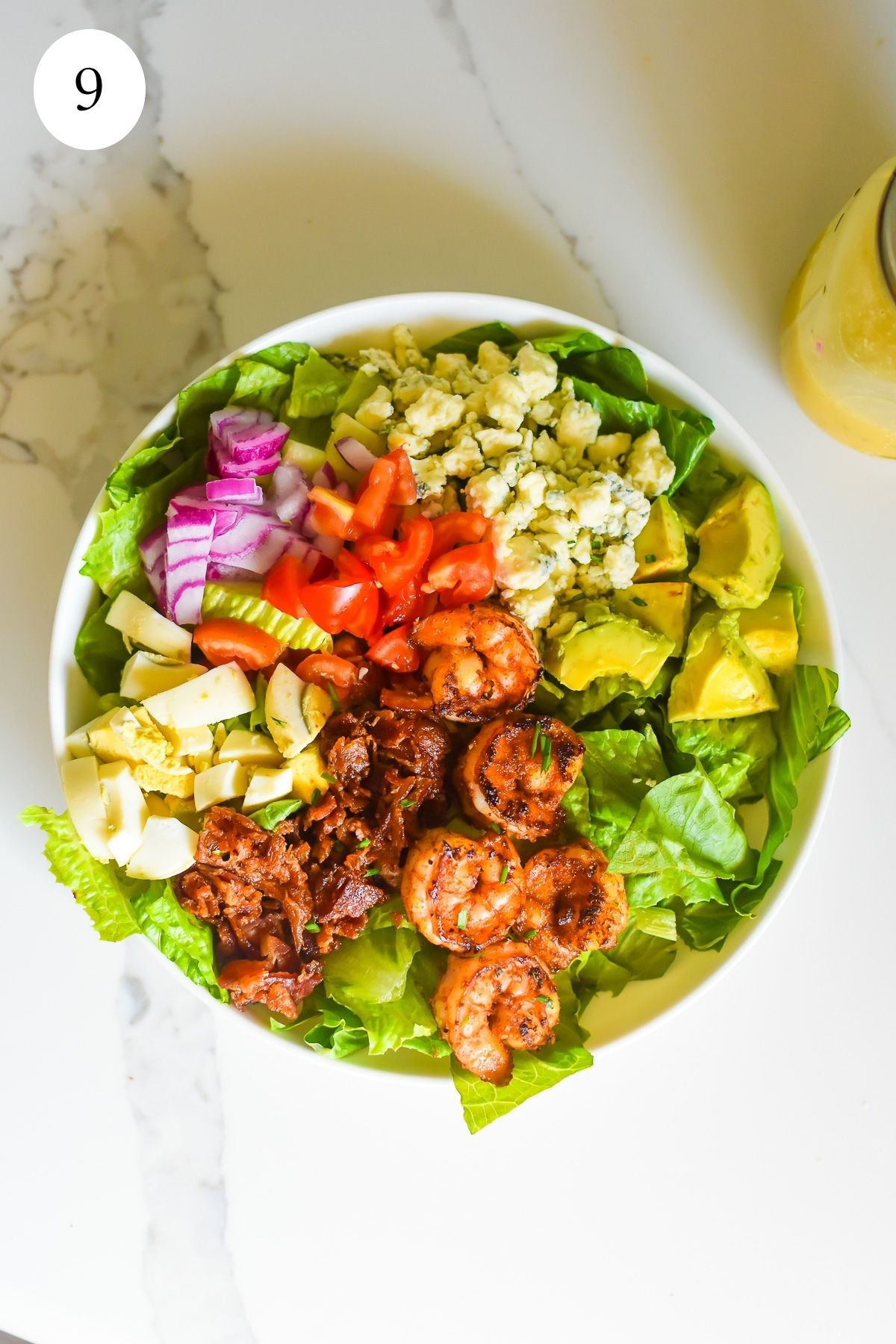 loaded cobb salad topped with crumbled gorgonzola cheese, diced red onions, tomatoes, avocado chunks, crumbled bacon, boiled egg, and blackened shrimps.