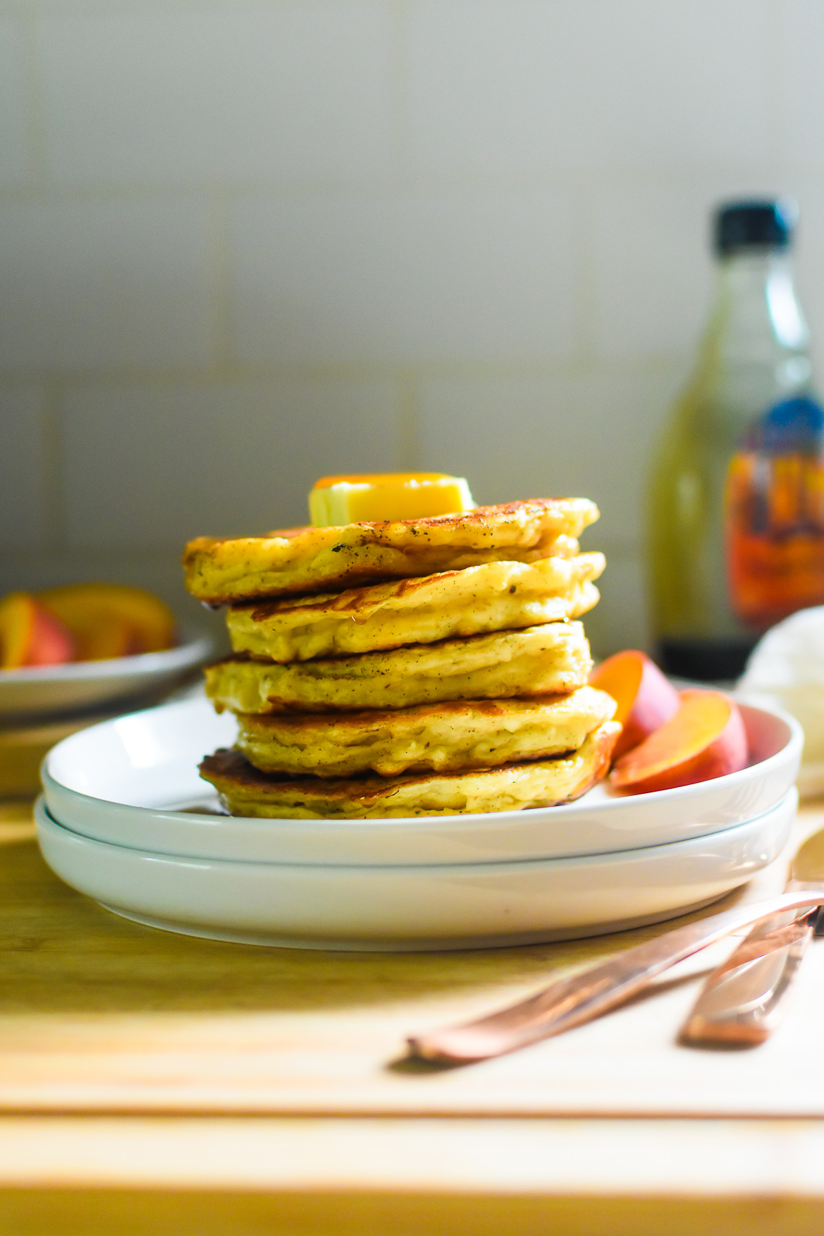 stack of the best, fluffiest Greek yogurt pancakes on white saucers topped with a thick pat of butter and amber-colored maple syrup.