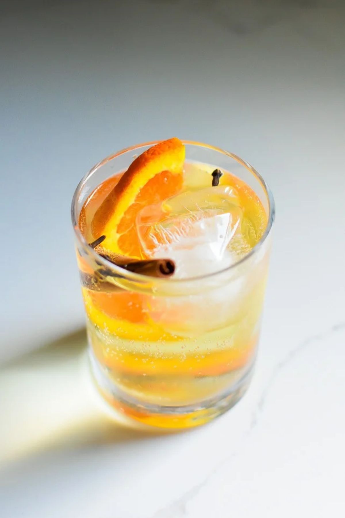 fall gin and tonic cocktail with apple cider, an orange slice, cinnamon stick, and whole cloves.
