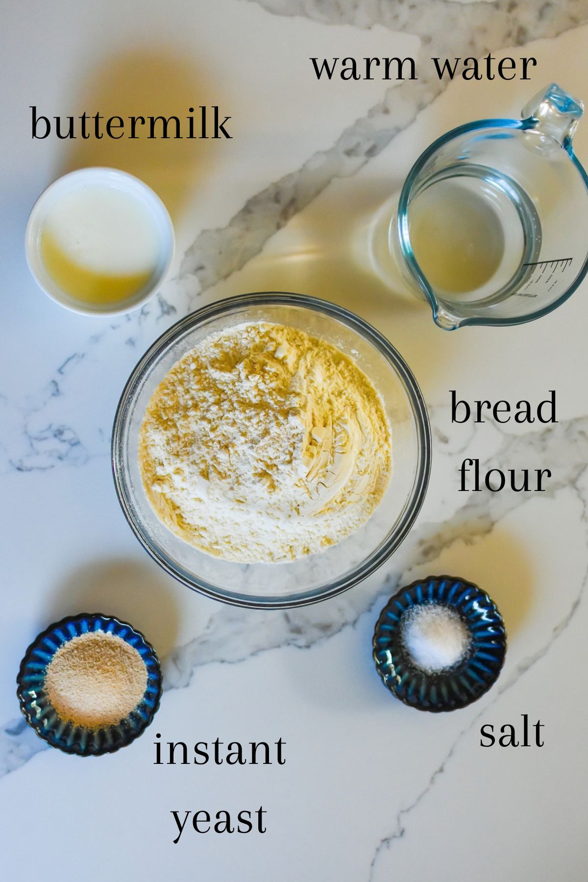 ingredients for a simple bread recipe with buttermilk on granite counter top: room temperature buttermilk, warm water, bread flour, yeast, and salt.