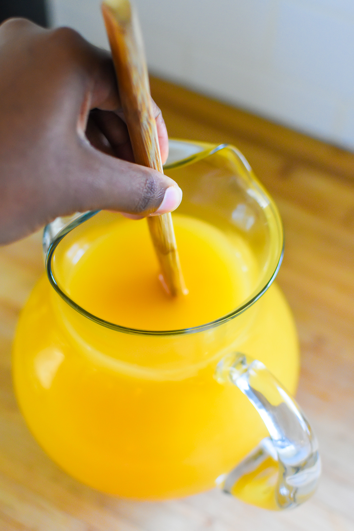 mixing orange juice with apple juice and ginger ale in a glass pitcher.