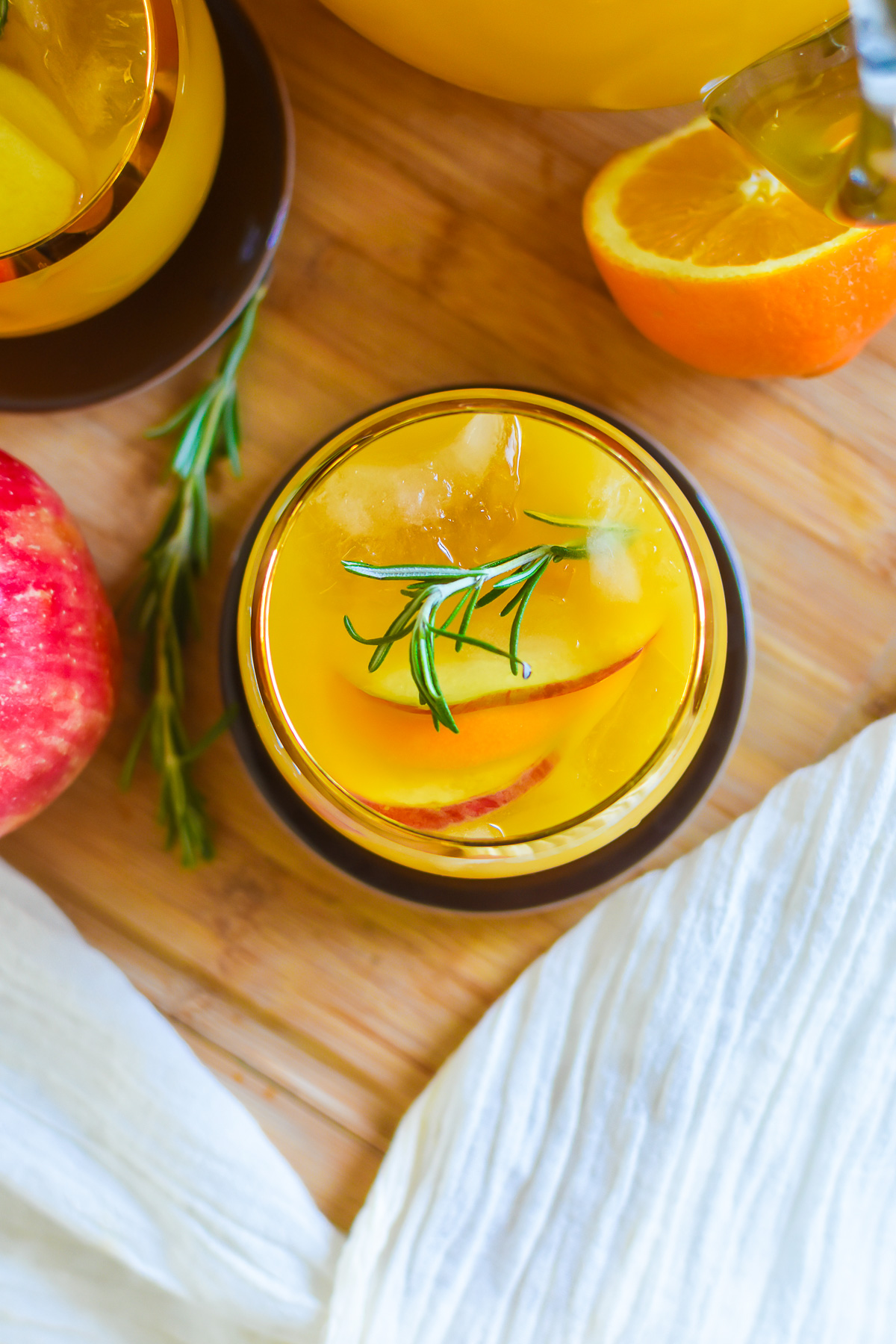 The best Thanksgiving punch with fresh apple and orange slices and a rosemary garnish.